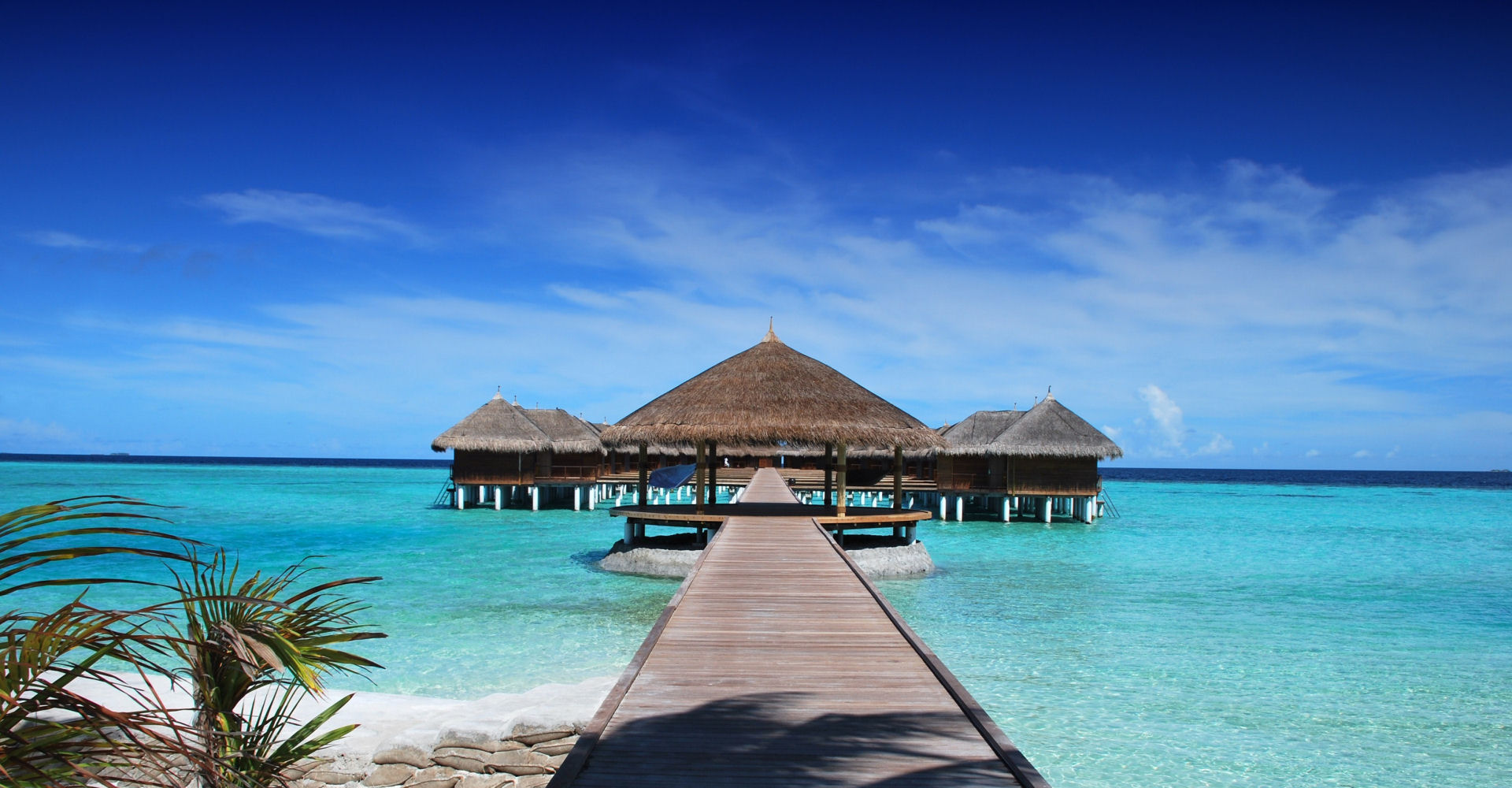 Bungalows sobre aguas turquesas y pasarela de madera hacia el mar
